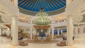 Un'ampia hall con un sontuoso lampadario, diverse zone relax e un soffitto alto decorato con un motivo blu.