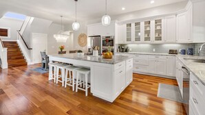 A modern kitchen with white cabinetry, a central island with stools, and a wooden staircase. - NEW LISTING - Nani Hale, 4 bed, AC, pool & jacuzzi (Koloa)