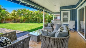 A covered patio area with wicker furniture, a glass table, and a view of a well-maintained lawn and palm trees. - NEW LISTING - Nani Hale, 4 bed, AC, pool & jacuzzi (Koloa)