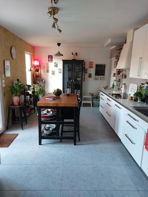 A modern kitchen with a wooden dining table, white cabinets, and a black cabinet with glass doors. - A 300 Metres de la Plage, Avec 5 Terrasses Maison Spacieuse et Lumineuse, (Bouzigues)