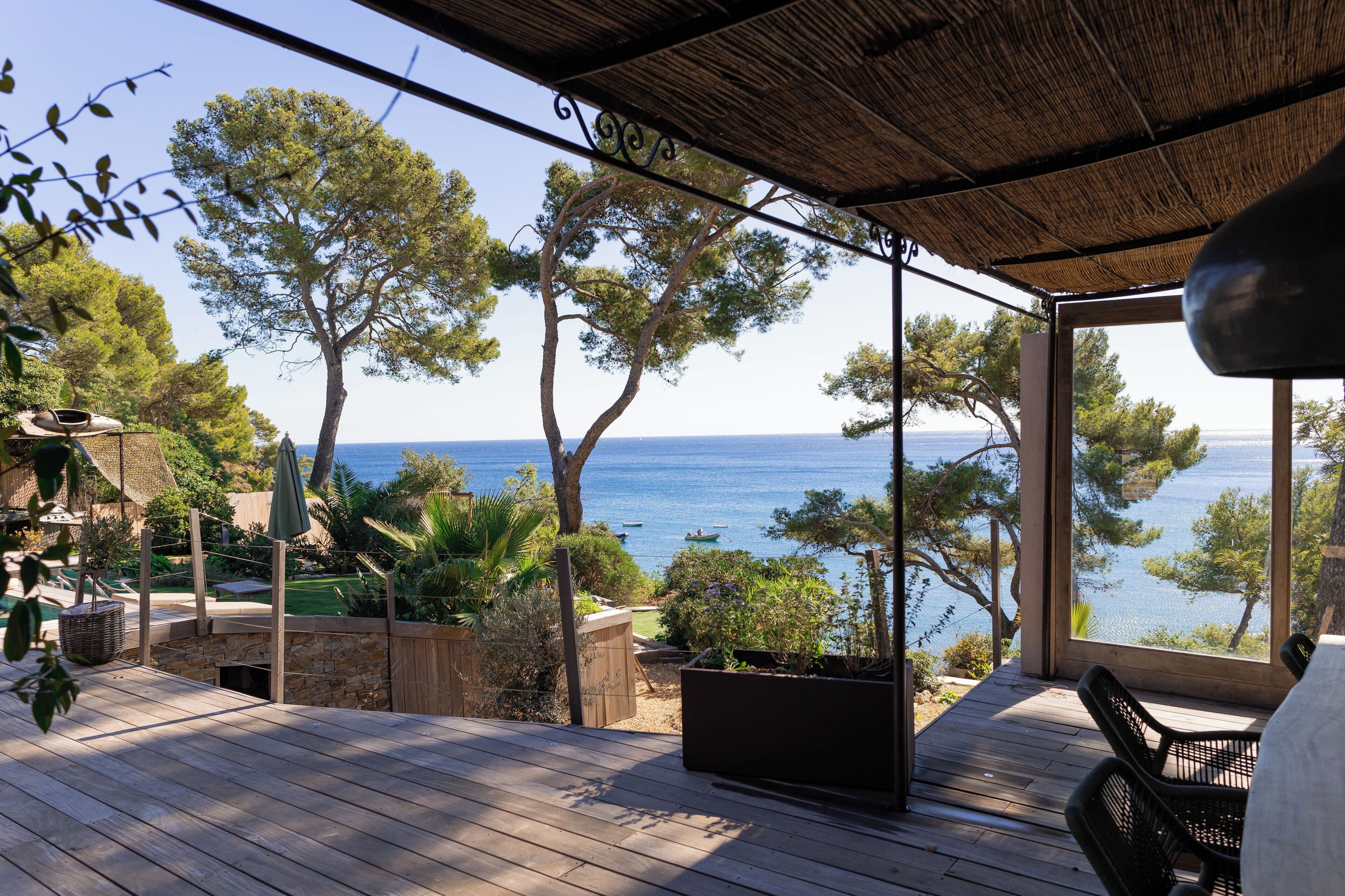 Een houten terras met uitzicht op zee, straatmeubilair en een pergola.