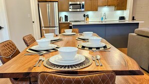 Un coin repas avec une table en bois dressée pour six personnes, entourée de fauteuils en cuir.