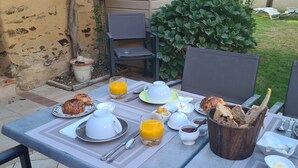 Un área de comedor al aire libre con una mesa preparada para el desayuno, incluyendo croissants, jugo y pan.