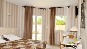 Una habitación de hotel con cama, escritorio, silla, lámpara y cortinas.