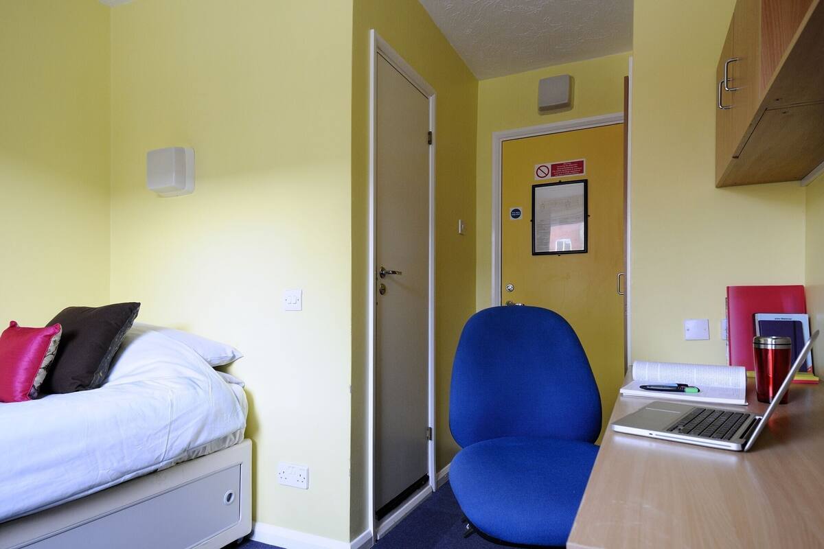 A room with a bed, a desk with a laptop, a chair, and a door.