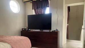 Een slaapkamer met een bed, een dressoir, een televisie en een raam met gordijnen.