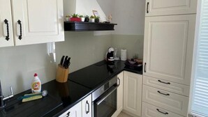 Een keuken met witte kastjes, een zwart aanrecht en een fornuis. Er staan planten op het aanrecht en er is een raam met zonwering.