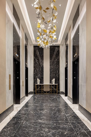 A modern hotel lobby with marble floors, a central reception desk, and a ceiling with hanging floral decorations.