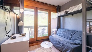 Ein kleines Zimmer mit Etagenbett, einer Schlafcouch, einem kleinen Tisch und einem Schreibtisch mit Lampe.