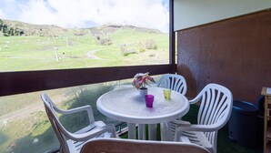 Ein Balkon mit Tisch und Stühlen, einer Topfpflanze und Blick auf eine grüne Landschaft mit Hügeln.