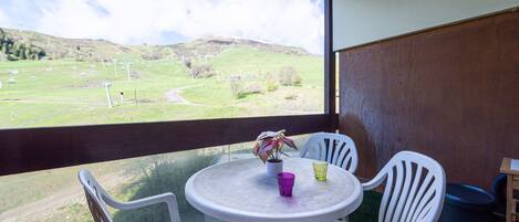 Ein Balkon mit Tisch und Stühlen, einer Topfpflanze und Blick auf eine grüne Landschaft mit Hügeln.