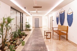 Experience the serene ambiance of this tranquil hallway, featuring a long, tiled floor, a small garden area, and a cozy bench for rest.