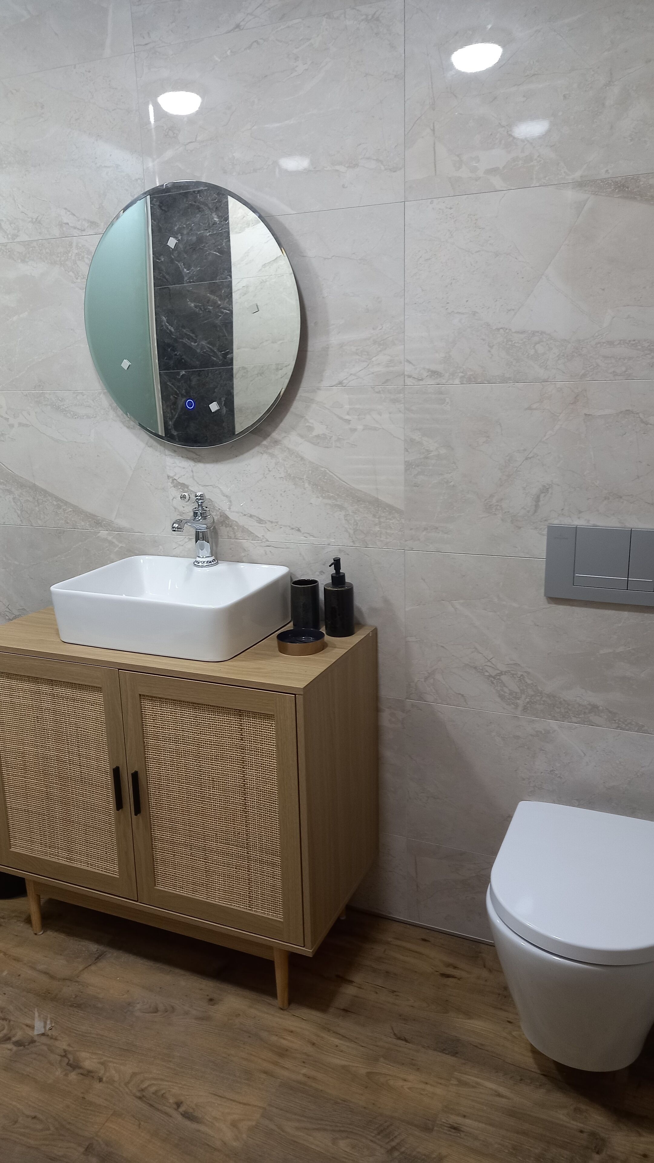 A bathroom with a white sink, a round mirror, a toilet, and a wooden cabinet.