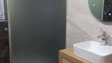 A modern bathroom with a glass shower enclosure, a wooden vanity with a sink, and a marble-tiled wall.