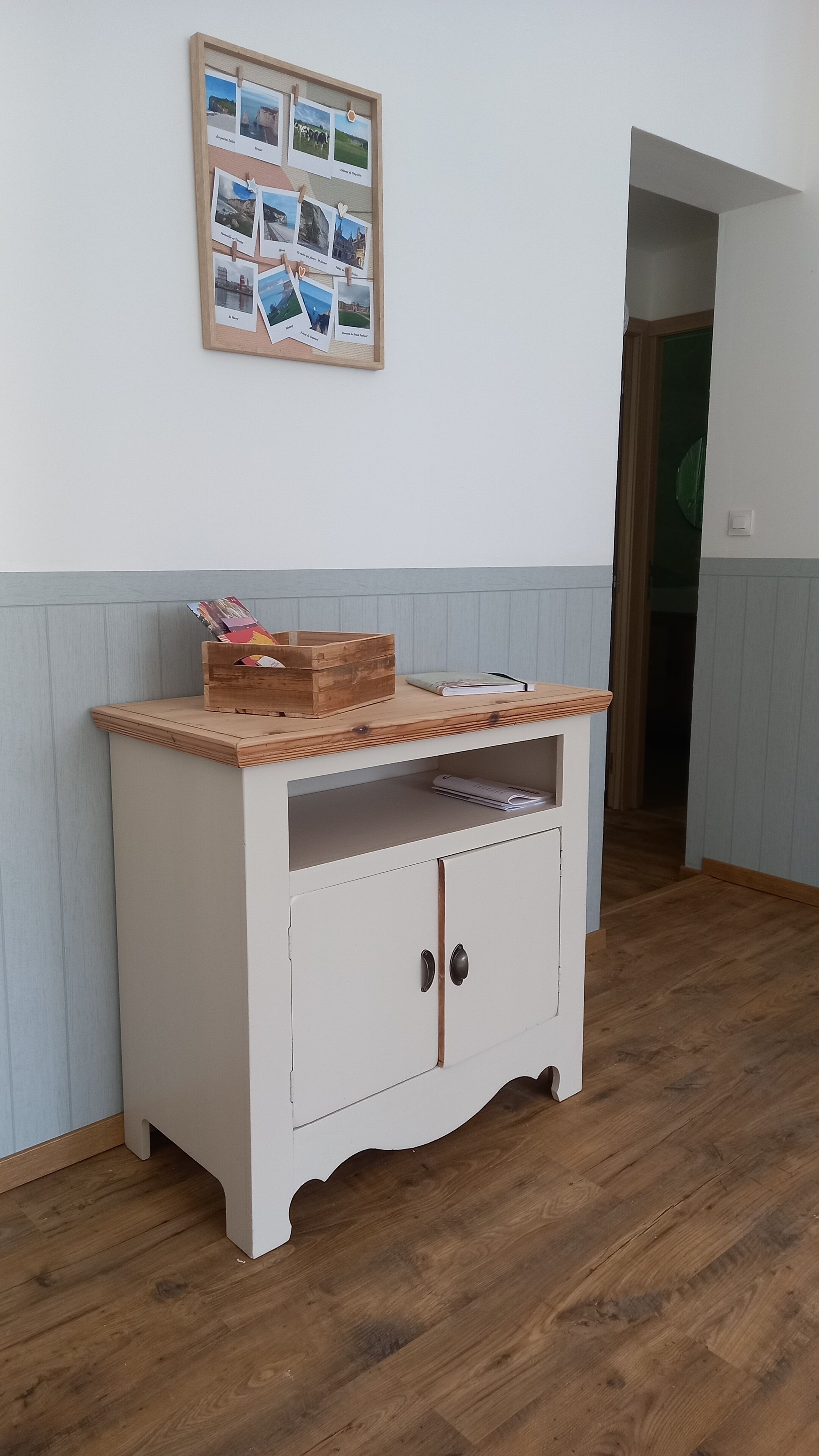 Un piccolo mobiletto in legno bianco con ripiano superiore in legno, un libro e una scatola di riviste.