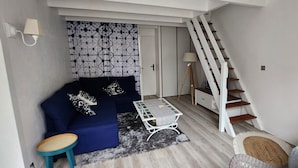 Een woonkamer met een bank, een salontafel, een stoel, een trap en een behang met patroon.