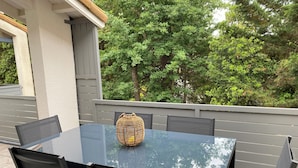 Een buitenpatio met een glazen tafel en zwarte stoelen, omringd door een grijze balustrade en begroeiing.