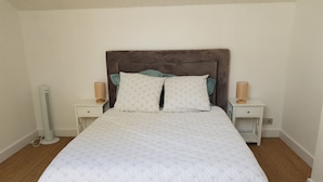 Een net opgemaakt bed met een bedsprei met patroon, twee kussens en een bruin hoofdbord. Er staan twee nachtkastjes met lampen en er is een vloerlamp.