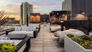 En takterrass med utomhusmöbler, utsikt över stadens silhuett och en modern byggnad i bakgrunden.
