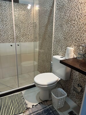 A modern bathroom with a glass shower enclosure, a toilet, a sink with a soap dispenser, and a trash bin. - Praia Comprida Flats (Angra dos Reis)