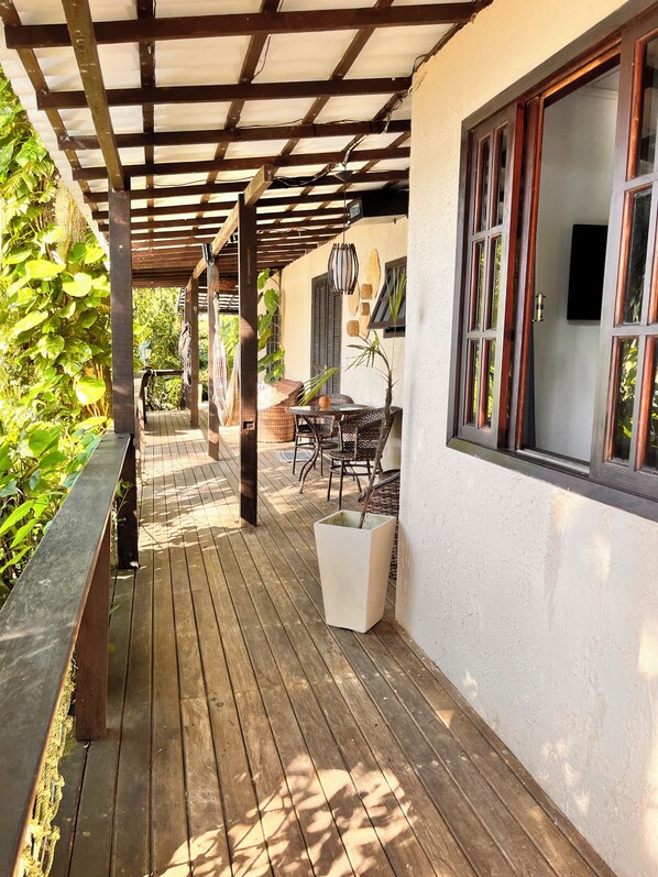 A wooden deck with outdoor furniture, a pergola, and a view of a building with windows and a door. - Praia Comprida Flats (Angra dos Reis)
