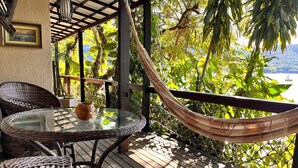 A wooden deck with wicker furniture, a hammock, and a glass table with a vase. - Praia Comprida Flats (Angra dos Reis)