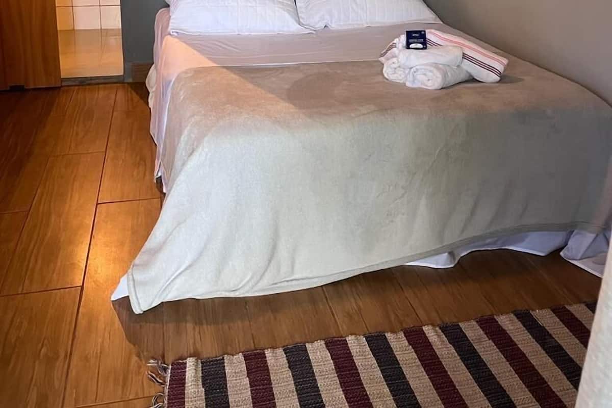 Makuuhuone, jossa on sänky, seinälle kiinnitetty puinen koriste-esine, valkoinen ilmastointilaite ja puulattia.
