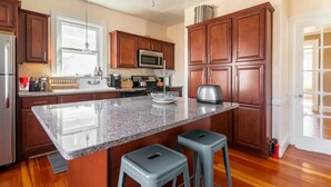 A modern kitchen with wooden cabinets, a granite countertop, and two bar stools. - Stylish comfortable period feature 2 bed - Sun drenched - Free parking (Providence)