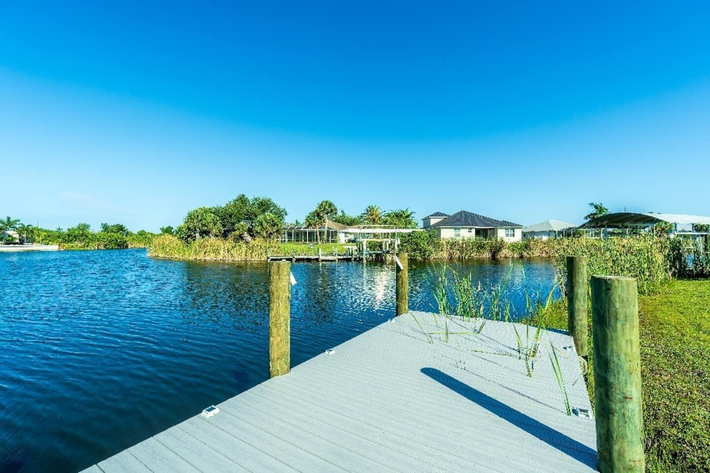 A waterfront property with a dock extending into a calm body of water, surrounded by greenery and residential buildings.