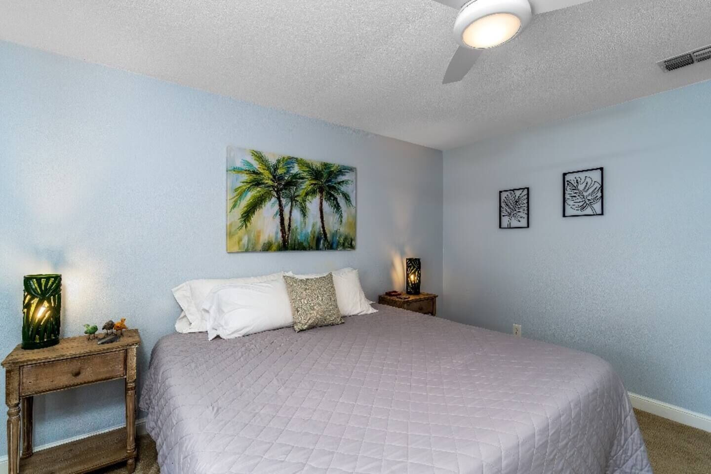 A bedroom with a large bed, two nightstands, a ceiling fan, and wall art.