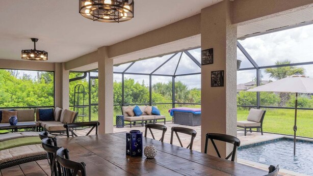 Eine großzügige Terrassenfläche mit Holztisch und -stühlen, einem Pool und einer überdachten Sitzgelegenheit mit Kissen.