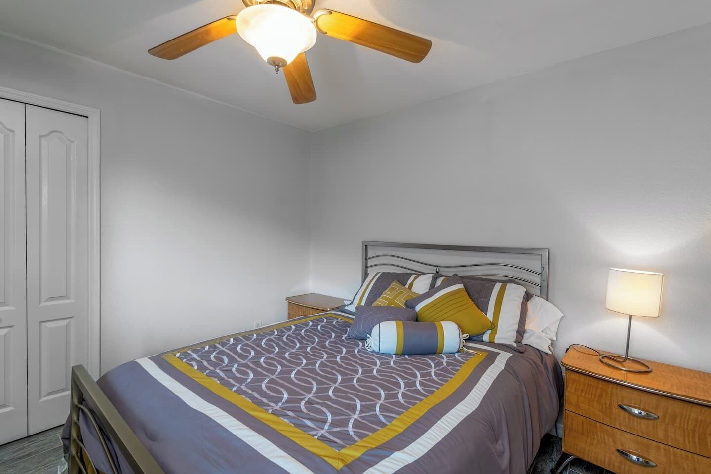 A bedroom with a bed, a nightstand, a lamp, and a ceiling fan.