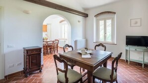 A dining area with a wooden table and chairs, a television on a stand, and a view of the kitchen through an archway. - Agriturismo Sant'elmira - Apt. Allegra w. Jacuzzi (Montescudaio)