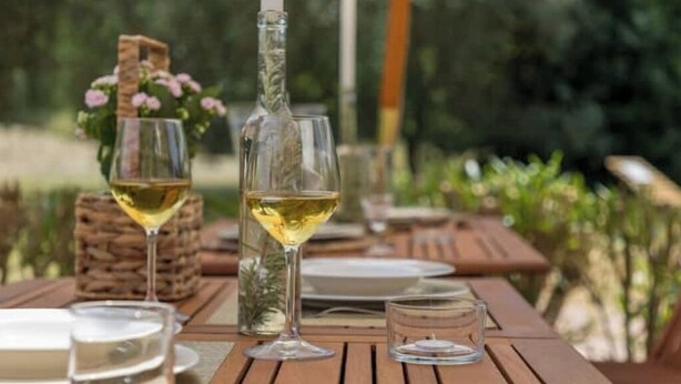 Una mesa de madera al aire libre con una botella de vino blanco, dos copas y una vela.