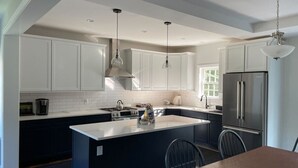 Una cocina moderna con armarios blancos, una isla central, electrodomésticos de acero inoxidable e iluminación colgante.