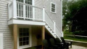 Una casa de dos pisos con un porche cubierto, una escalera y mobiliario exterior.