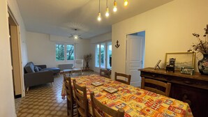 A dining area with a patterned tablecloth, wooden chairs, a ceiling fan, and a view of the outdoors through windows. - La marmotte - Holiday home - Les Mathes (Les Mathes)