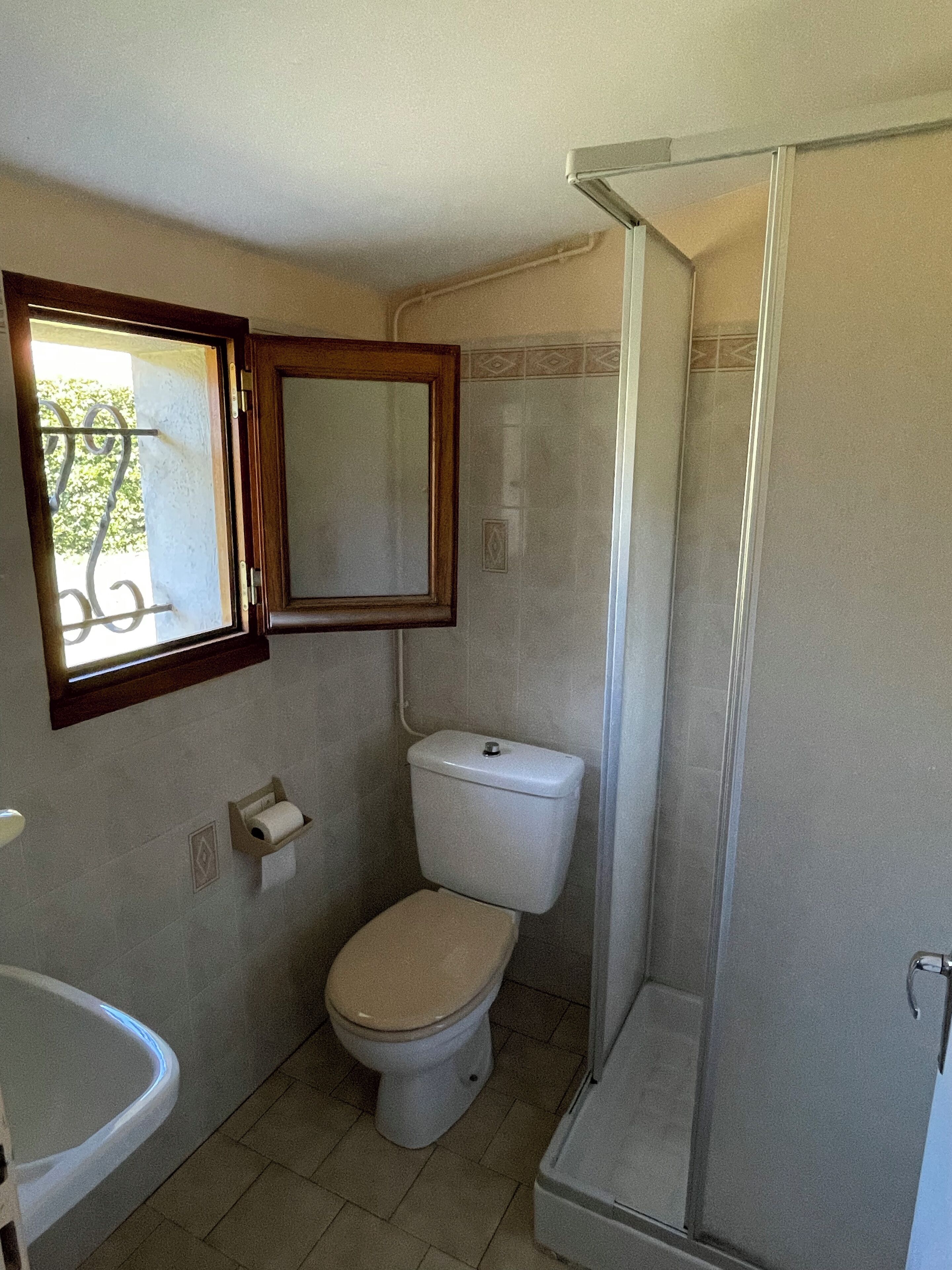 Ein Badezimmer mit Toilette, Waschbecken, Dusche und einem Fenster mit Zierrahmen.