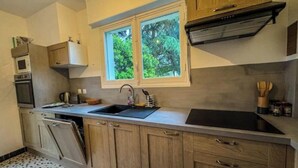 A compact kitchen with wooden cabinets, a double sink, and a window with a view of greenery. - La marmotte - Holiday home - Les Mathes (Les Mathes)