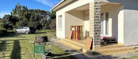 A single-story house with a covered porch, a stone pillar, and a small outdoor seating area.