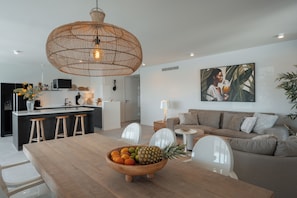A modern kitchen with a central island, a dining area with a wooden table and chairs, and a living area with a sofa and a painting on the wall.