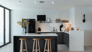 A modern kitchen with a large island, bar stools, a flat-screen TV, and a herringbone-patterned backsplash.