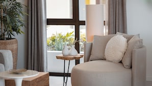 A modern living room with a sofa, a side table, a lamp, and a potted plant.