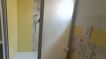 A bathroom with a toilet, a shower with a patterned door, and a tiled wall with a floral design.