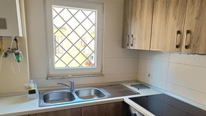 A kitchen with a double sink, wooden cabinets, a window with a grid pattern, and a black stove. - In the Hospital Zone of Naples. (Napoli)