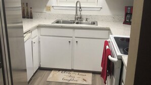 A kitchen with white cabinets, a stainless steel refrigerator, a double sink, and a red towel hanging on the oven.