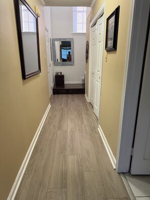 A hallway with wooden flooring, white doors, and a mirror on the wall.
