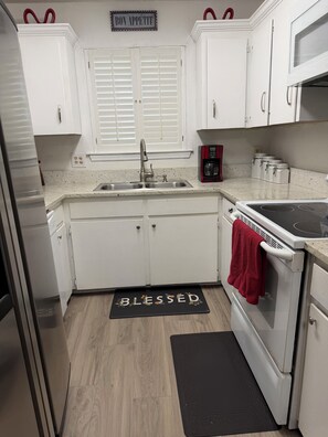 A kitchen with white cabinets, a stainless steel sink, a stove, and a microwave.