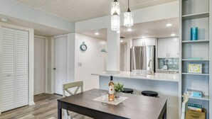 A modern kitchen with stainless steel appliances, a dining area with a wooden table, and pendant lighting. - Ocean and Racquet #5217 (St. Augustine)