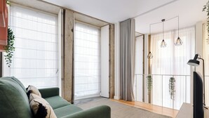 A modern living room with a green sofa, a flat-screen TV, and large windows with sheer curtains. - Sbucks - Trendy Space in Porto - Next to Ribeira (Porto)